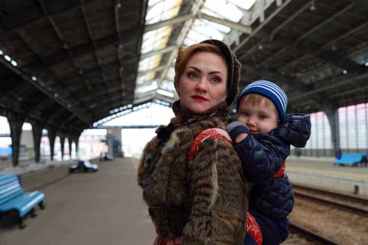 Woman with baby carrier in warm coat at train station