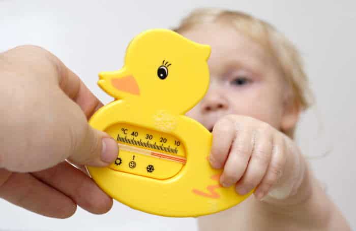 a baby holding a duck bath thermometer