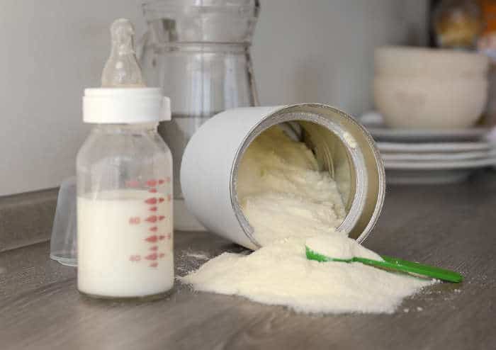 A baby formula tin and bottle with spilt formula powder
