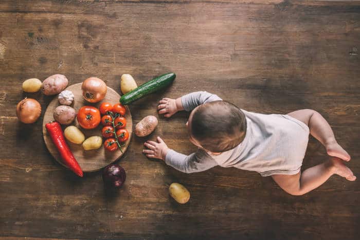 A baby crawling towards a selection of vegetables