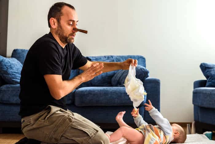 A dad with a peg on his nose changing babies diaper