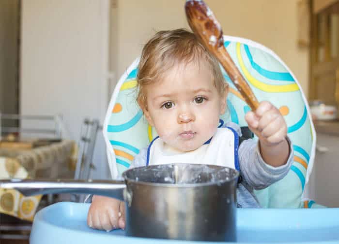 Baby self-feeding with large wooden spoon and pan