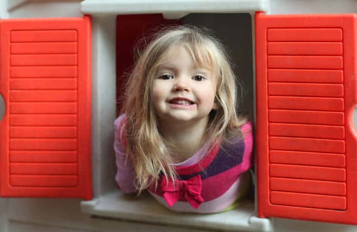 Little girl leaning out the window of her plastic playhouse