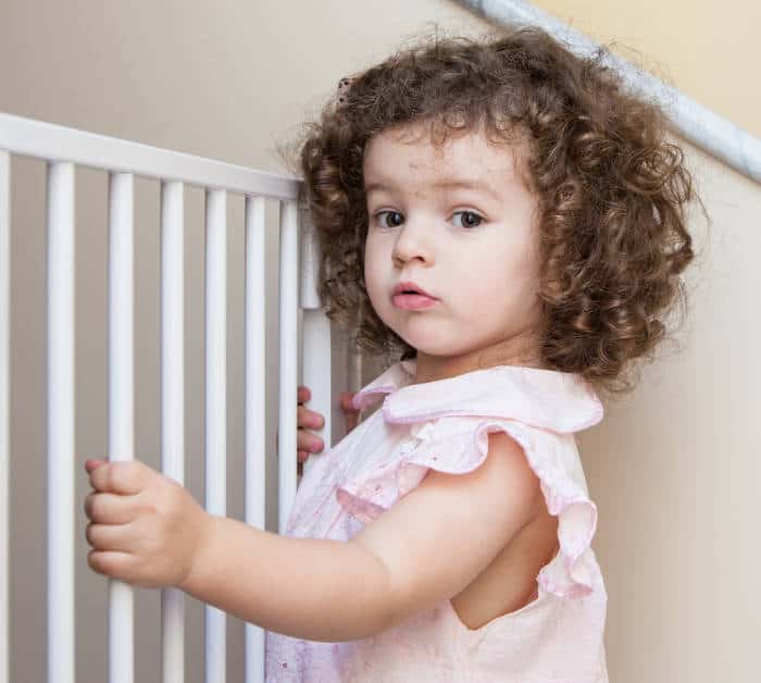 cute toddler girl standing at a baby safety gate