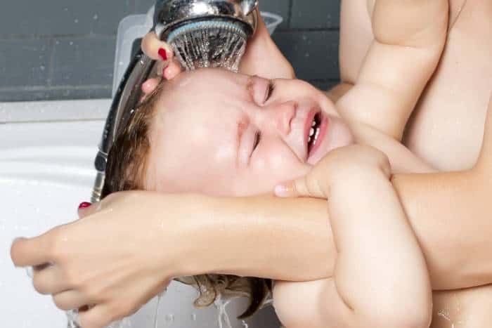 baby having hair washed under a shower head